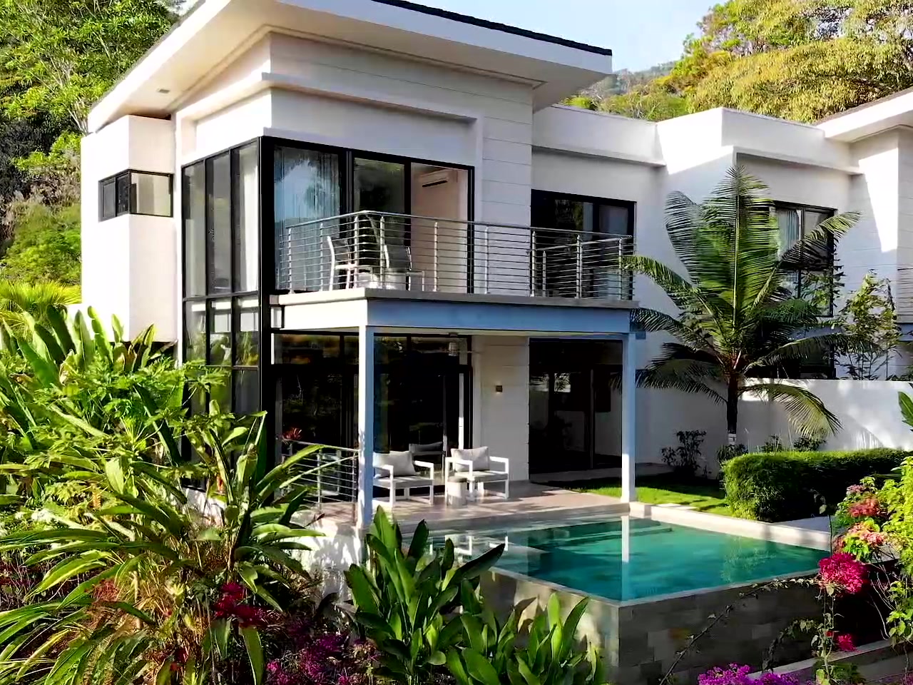 A villa at The Terraces of San Martín — two storeys of glass and white walls above a plunge pool, heliconia and bougainvillea in the foreground and a neighbouring villa beyond