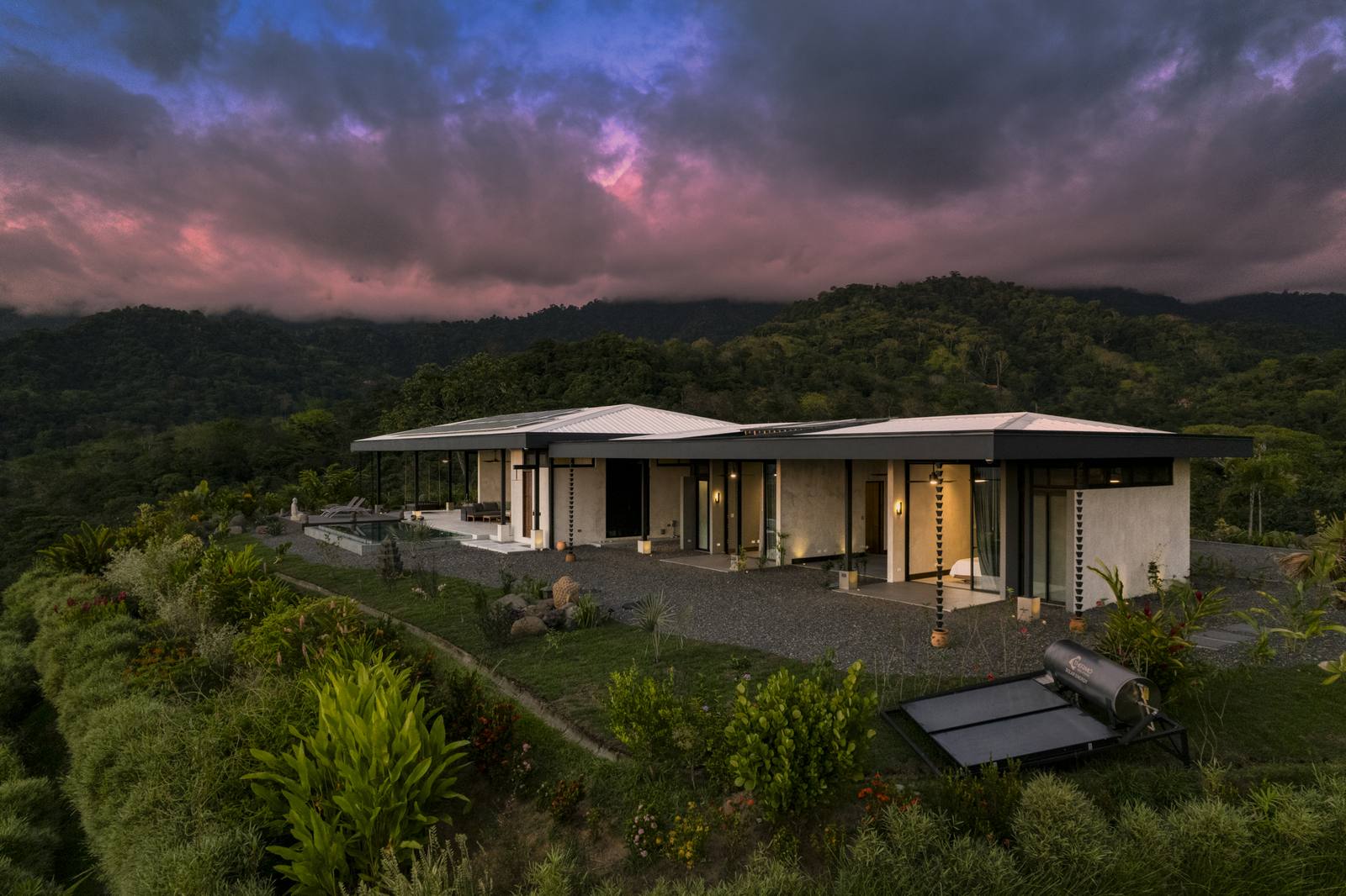 Casa Karuna &mdash; The house at dusk from the air, lit under a violet sky