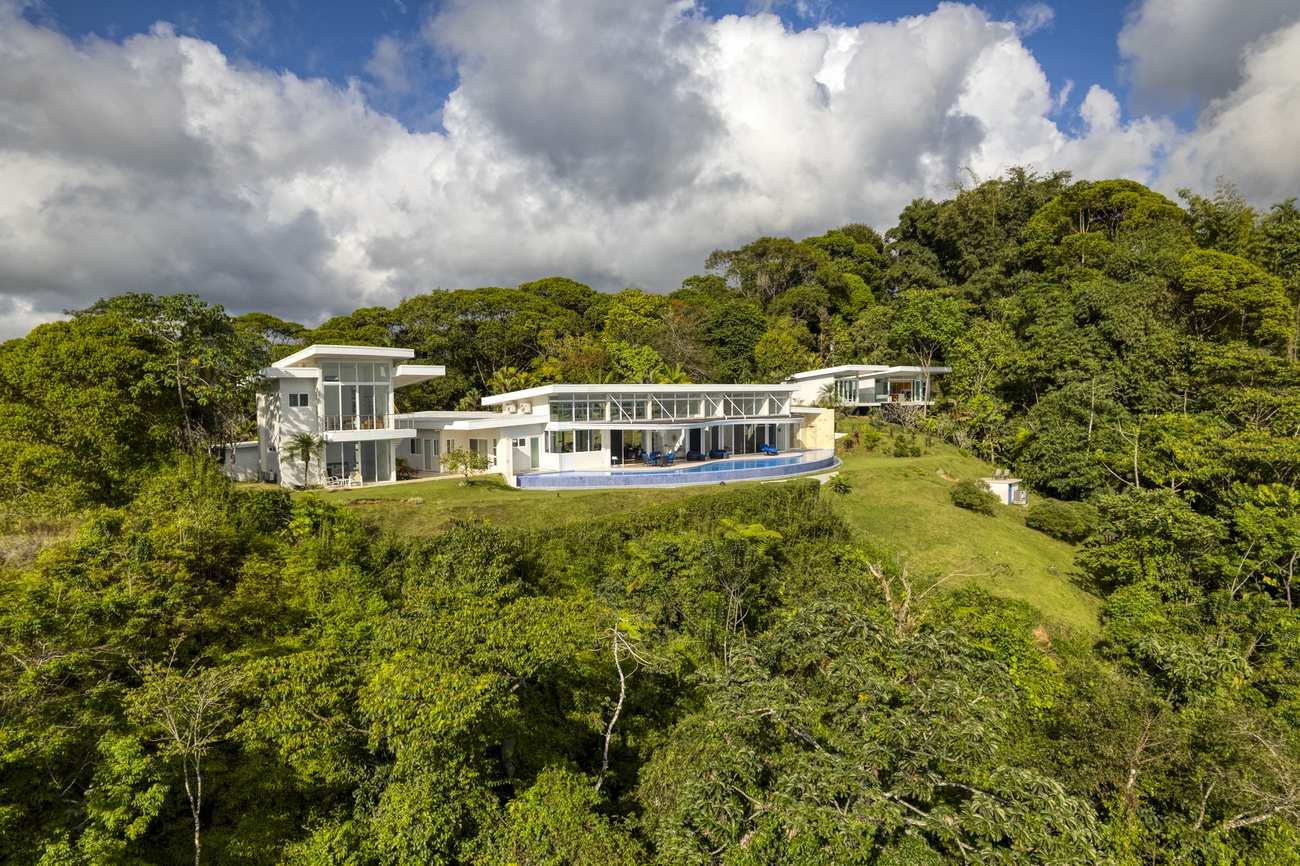 The house seen from the hillside above, long and low against the rainforest