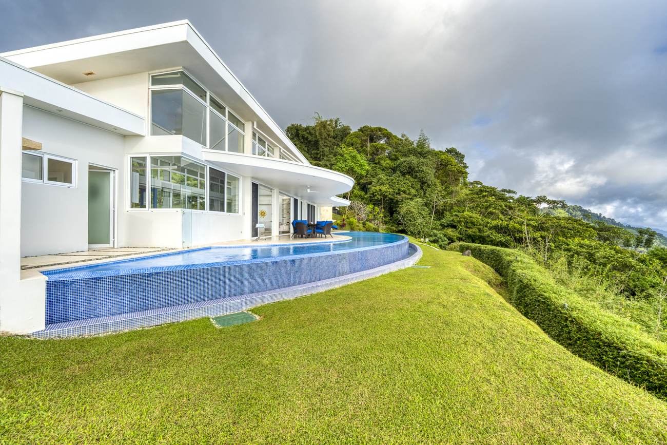 The curved infinity pool wrapping the covered terrace, seen from the lawn