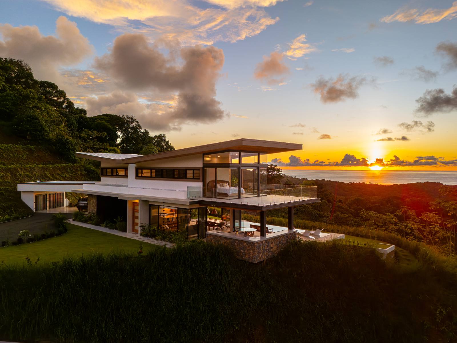 A modern glass estate lit at dusk above Ojochal, the sun setting over the Pacific behind it